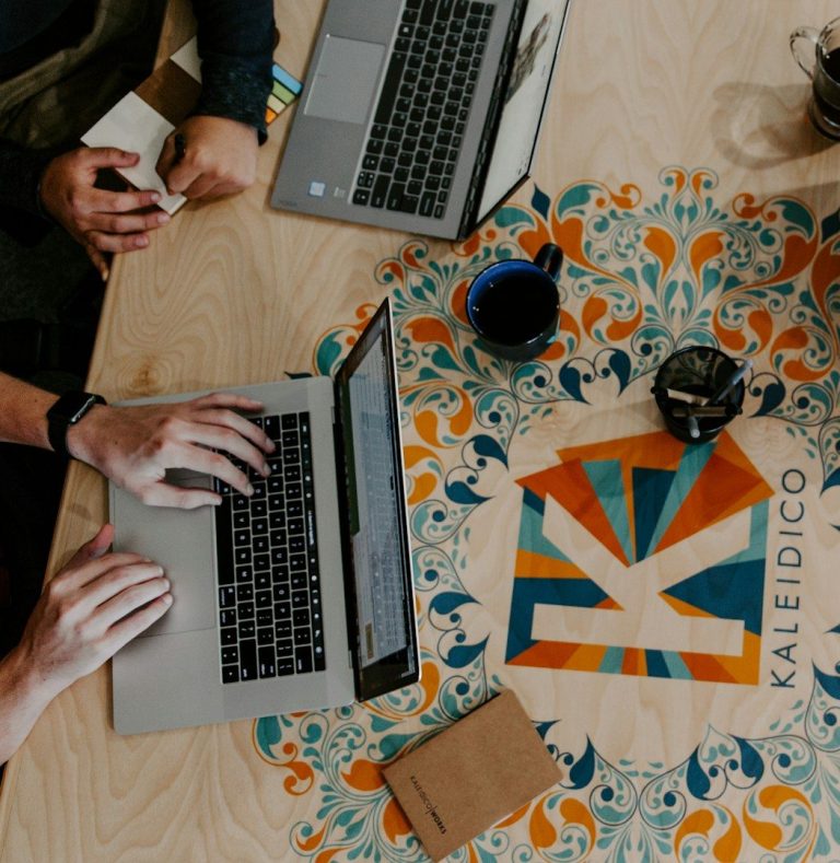 Strategic Development Hands typing on laptops, with a colourful table design and coffee cups.